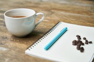 image of cup of coffee and a notebook with pen on top of it