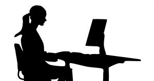 silhouette of young woman sitting and typing on pc 
