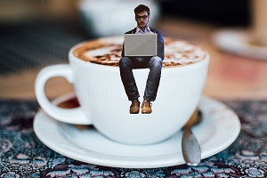 man working on a pc sitting on top of a coffee cup